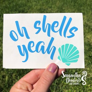 May include: A white vinyl sticker with the text "Oh shells yeah" in blue lettering and a teal seashell graphic.