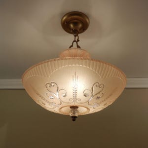 Pode incluir: Uma lumin&aacute;ria de teto com uma c&uacute;pula larga de vidro fosco rosa p&aacute;lido e borda canelada. O vidro &eacute; decorado com volutas e padr&otilde;es florais prateados gravados, suspensa por um dossel e corrente em tom de bronze met&aacute;lico.