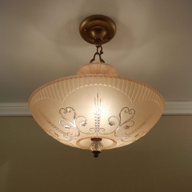 Pode incluir: Uma lumin&aacute;ria de teto com uma c&uacute;pula larga de vidro fosco rosa p&aacute;lido e borda canelada. O vidro &eacute; decorado com volutas e padr&otilde;es florais prateados gravados, suspensa por um dossel e corrente em tom de bronze met&aacute;lico.