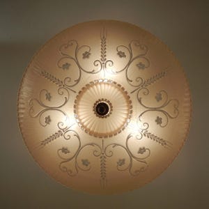 Pode incluir: Uma lumin&aacute;ria de teto circular de vidro fosco com um tom quente de p&ecirc;ssego. A superf&iacute;cie apresenta um padr&atilde;o gravado de vinhas florais sim&eacute;tricas e caules de trigo que irradiam de um medalh&atilde;o central de vidro canelado.