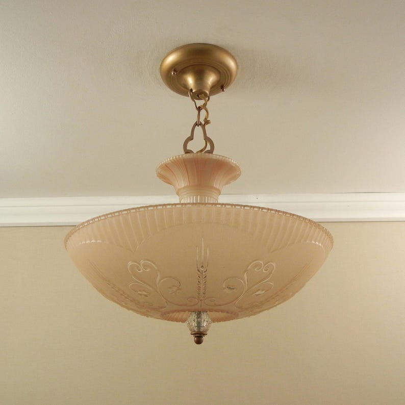 Pode incluir: Uma lumin&aacute;ria de teto com uma c&uacute;pula de vidro fosco em rosa p&aacute;lido, apresentando padr&otilde;es gravados de volutas e espigas. A pe&ccedil;a inclui uma base de metal em tom de lat&atilde;o, uma corrente decorativa e um pequeno remate de vidro transparente.