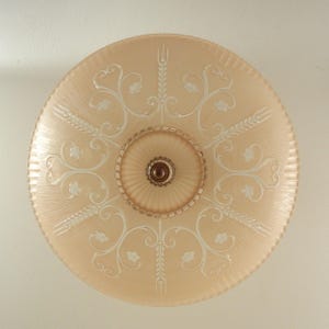 Pode incluir: Uma lumin&aacute;ria de teto redonda de vidro cor de p&ecirc;ssego com uma c&uacute;pula central canelada e um remate castanho escuro. O abajur de vidro &eacute; decorado com espigas de trigo e padr&otilde;es de volutas gravados em branco, com uma borda exterior estriada.