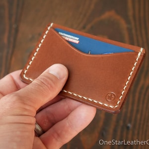 May include: A brown leather card holder with a white stitch detail and a small star logo. A blue card is partially visible inside the holder.