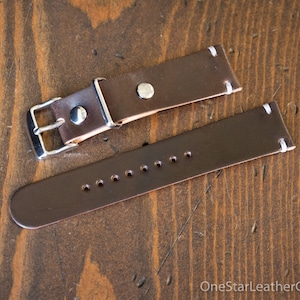 May include: A brown leather watch strap with white stitching and a silver buckle. The strap has multiple holes for adjusting the size.