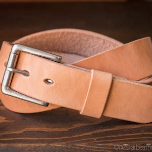 May include: A light brown leather belt with a silver buckle. The belt is folded in half and the buckle is visible.