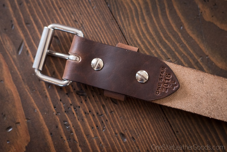 May include: A brown leather belt with a silver buckle and a brown leather strap. The strap has the text "ONE STAR 2016" embossed on it.