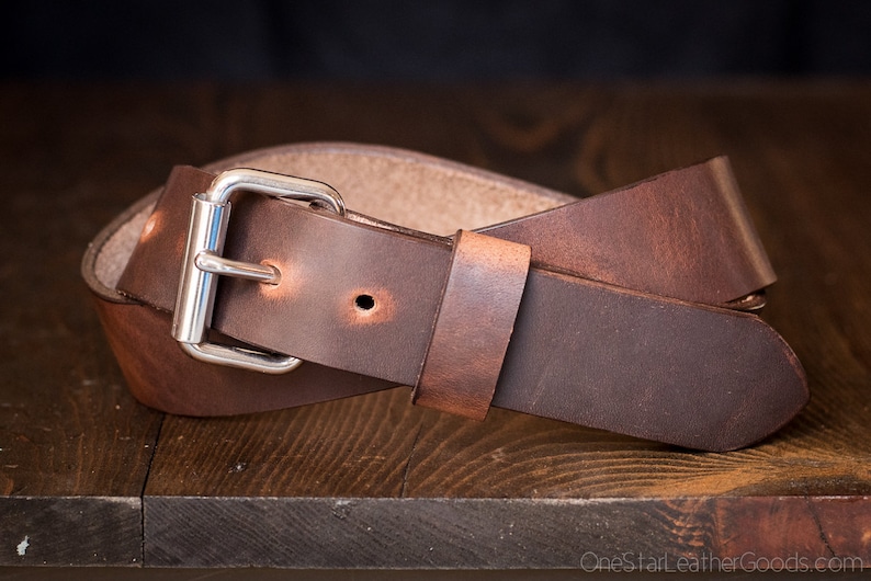 May include: A brown leather belt with a silver buckle. The belt is folded in half and the buckle is visible in the center of the image.