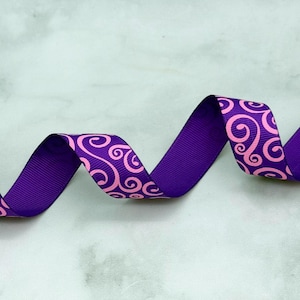 May include: A length of purple grosgrain ribbon featuring a repeating pattern of light pink swirls. The ribbon is arranged in a series of gentle, flowing curves, showcasing the textured ribbed surface and the consistent graphic print design.
