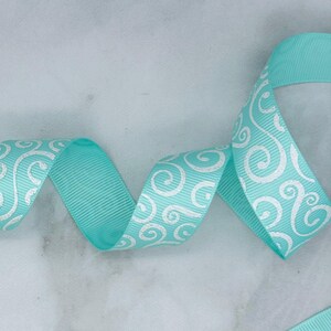 May include: A turquoise grosgrain ribbon featuring a repeating white swirl pattern. The ribbon has a distinct ribbed texture and is shown in a loose, winding S-curve shape, displaying the consistent pattern across its length.
