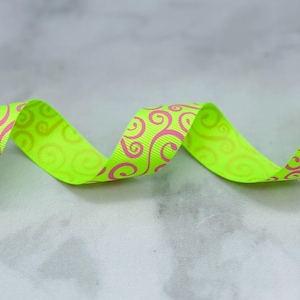 May include: A neon yellow grosgrain ribbon featuring a repeating pattern of hot pink swirls. The ribbon is arranged in a gentle, undulating wave shape, showcasing the textured fabric surface and the vibrant contrast between the bright yellow and pink.