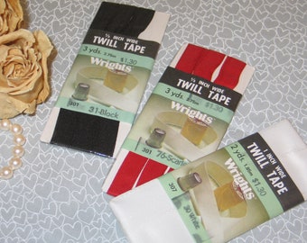 May include: Three packages of Wrights twill tape in black, red, and white. Each package is labeled with the width, length in yards and meters, and the price. The black tape is 1/2 inch wide and 3 yards long. The red and white tapes are 1 inch wide.
