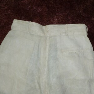 May include: A pair of white linen pants with a back pocket. The pants have a waistband with a button closure.