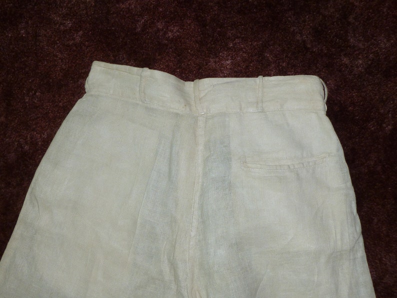 May include: A pair of white linen pants with a back pocket. The pants have a waistband with a button closure.