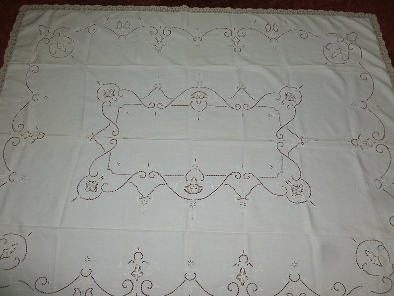 K&ouml;nnte beinhalten: Wei&szlig;e bestickte Tischdecke mit einem zarten Blumenmuster. Die Tischdecke hat einen geh&auml;kelten Rand und ist aus feinem Leinenstoff gefertigt.