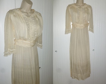 May include: A vintage ivory-coloured dress with a lace bodice and a sash. The dress has a long, flowing skirt and three-quarter sleeves.