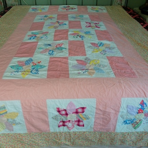 May include: A pink patchwork quilt with a floral design. Each square features a different coloured flower with a variety of fabrics. The quilt is made with a variety of fabrics, including cotton and linen.