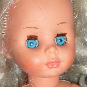 Puede incluir: Una mu&ntilde;eca de porcelana con el pelo largo y blanco y ojos azules. La mu&ntilde;eca tiene una sonrisa pintada y mejillas sonrosadas.