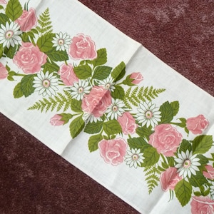 Könnte beinhalten: Weißer Tischläufer mit floralem Muster aus rosa Rosen, weißen Gänseblümchen und grünen Blättern. Der rechteckige Läufer ist aus Stoff. Das florale Design ist auf den Stoff gedruckt.