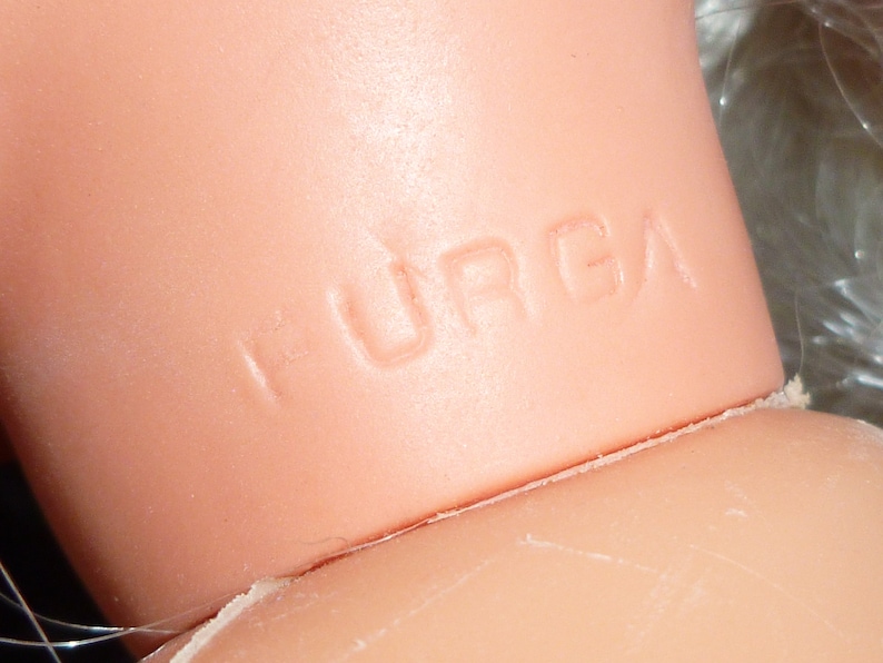 Puede incluir: Primer plano del cuello de una mu&ntilde;eca con la palabra "HURGA" en relieve en la piel.
