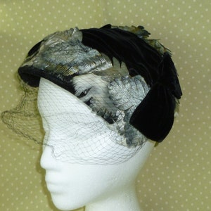 May include: A black velvet hat with silver feather accents and a black netting veil.