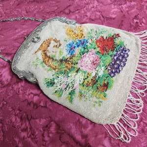May include: A vintage beaded purse with a floral design and a silver chain. The purse has a fringe of beads around the bottom.