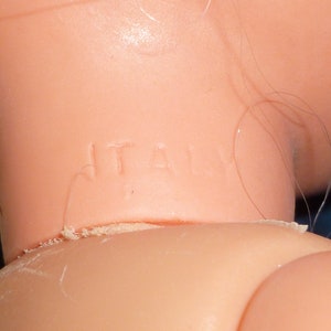 Puede incluir: Primer plano del cuello de una mu&ntilde;eca con la palabra "ITALIA" estampada.