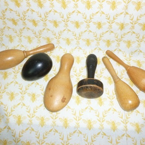 May include: A collection of seven wooden tools for crafting, including a mallet, a small hammer, and a round, black tool. The tools are arranged on a white fabric with a yellow bee pattern.