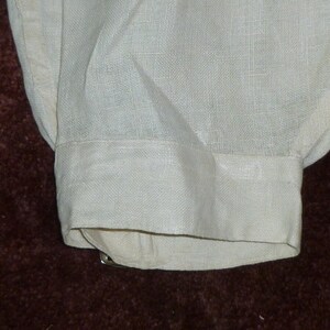 May include: A white linen shirt cuff with a folded edge. The cuff is made of a soft, lightweight fabric.
