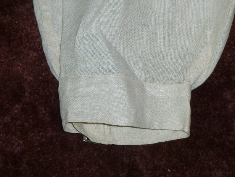 May include: A white linen shirt cuff with a folded edge. The cuff is made of a soft, lightweight fabric.