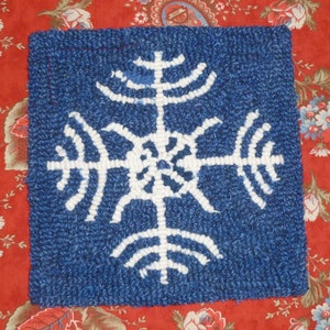 Op de afbeelding: Een handgestikt blauw en wit kleed met een sneeuwvlokdesign. De sneeuwvlok is wit en de achtergrond is blauw.