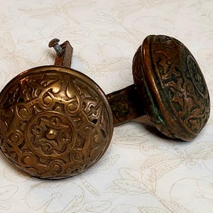 Peut inclure: Deux boutons de porte en laiton antique avec des motifs floraux complexes. Les boutons sont reliés par une barre en métal.