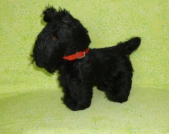 May include: Black plush toy dog with a red collar. The dog is standing on a green background.