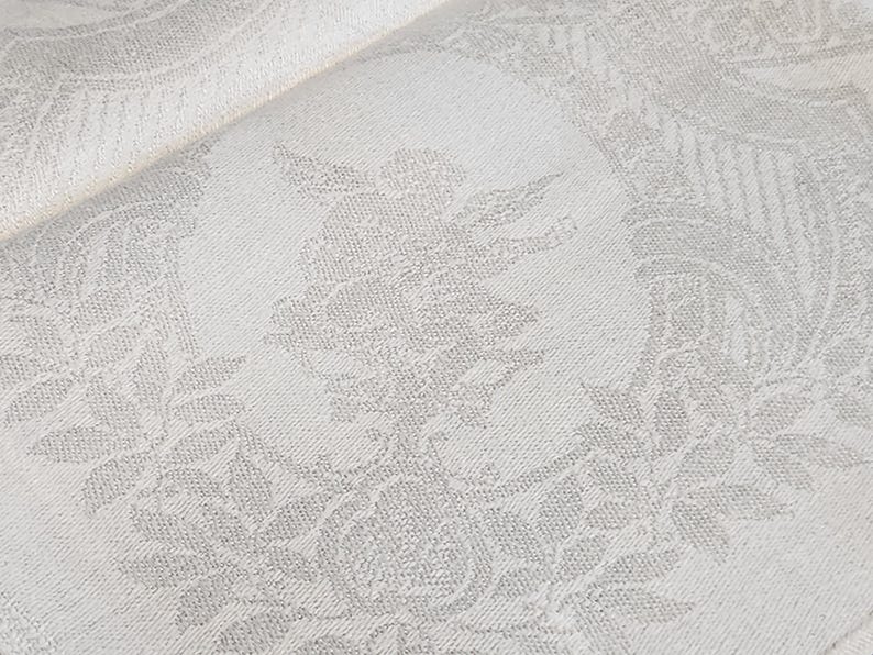 Op de afbeelding: Witte stof met een subtiel reli&euml;fpatroon van bladeren en bloemen. De stof heeft een zachte, textuur.
