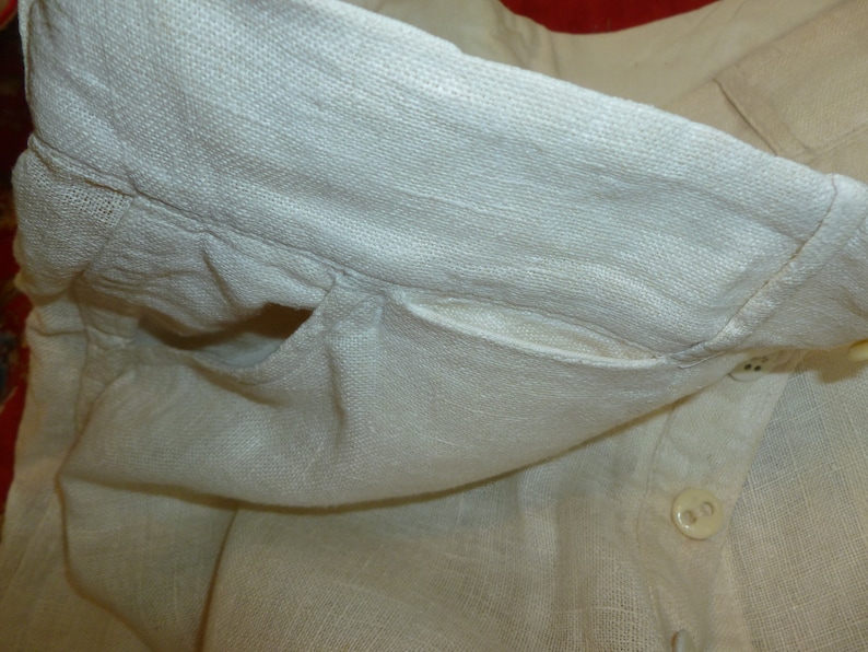 May include: A white linen shirt with a pocket and a button closure. The shirt is folded over and the pocket is visible.