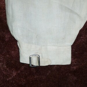 May include: A white linen shirt cuff with a silver metal buckle.