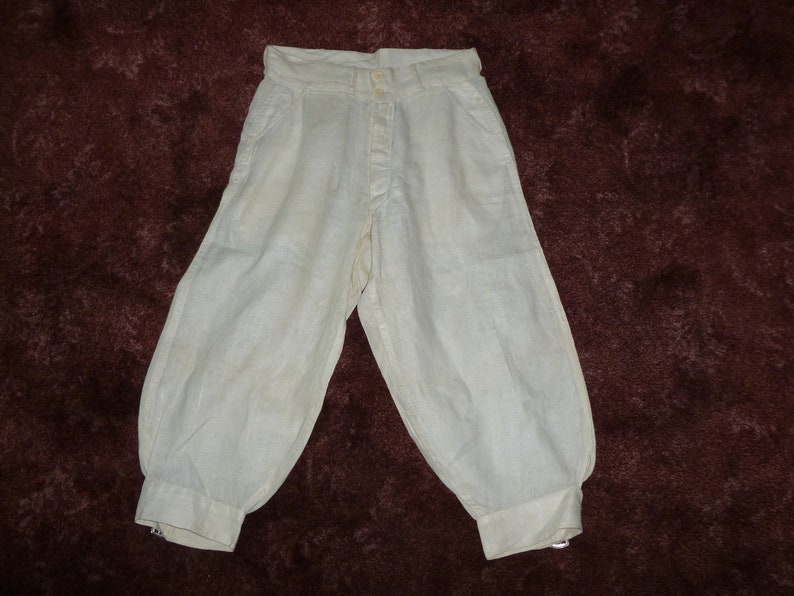 May include: White linen pants with a button fly and a gathered cuff at the bottom.