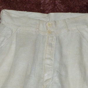 May include: White linen pants with a button fly and two front pockets.