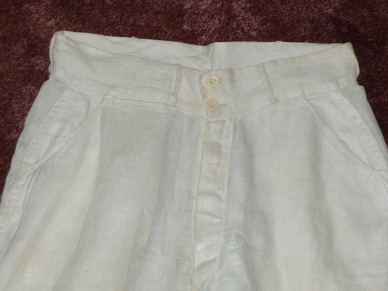May include: White linen pants with a button fly and two front pockets.