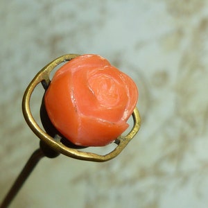 May include: A vintage coral rose pin with a brass setting. The rose is carved in detail and has a delicate, feminine design.