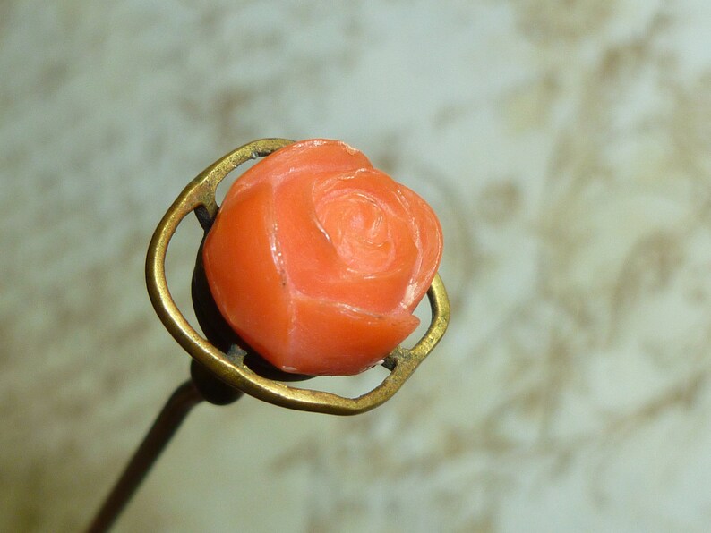 May include: A vintage coral rose pin with a brass setting. The rose is carved in detail and has a delicate, feminine design.