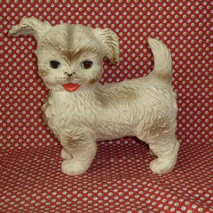 Peut inclure: Un chien en peluche blanc et brun avec un nez et une langue roses. Le chien est assis sur un tissu à pois rouges et blancs.