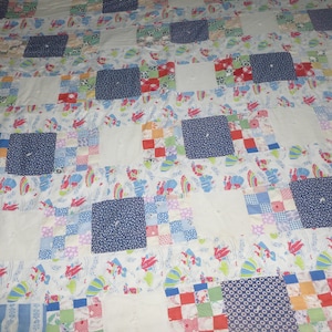 May include: A vintage quilt with a patchwork design featuring squares of various colors and patterns, including blue, red, green, and white. The quilt is made of cotton fabric and has a white background.