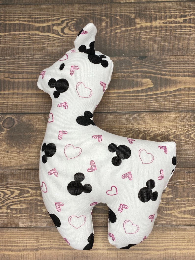 Puede incluir: Juguete de peluche blanco con forma de llama con un estampado de Mickey Mouse en blanco y negro y corazones rosas.