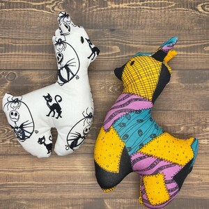 May include: Two plush toys, one white with black details and the other multi-colored with a patchwork design. Both toys are shaped like a llama.