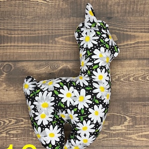 May include: A black and white stuffed llama with a daisy print. The llama is standing on a wooden surface.