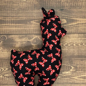 Puede incluir: Un juguete de peluche de alpaca negro con lunares rojos y lazos rojos. La alpaca est&aacute; de pie sobre una superficie de madera.