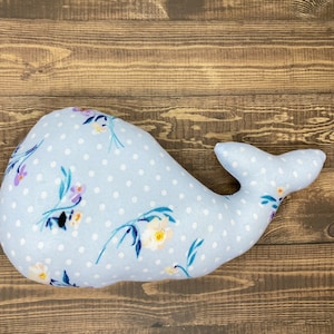 May include: A light blue whale-shaped pillow with a white polka dot pattern and a floral print. The pillow is made of soft fabric and is perfect for cuddling.