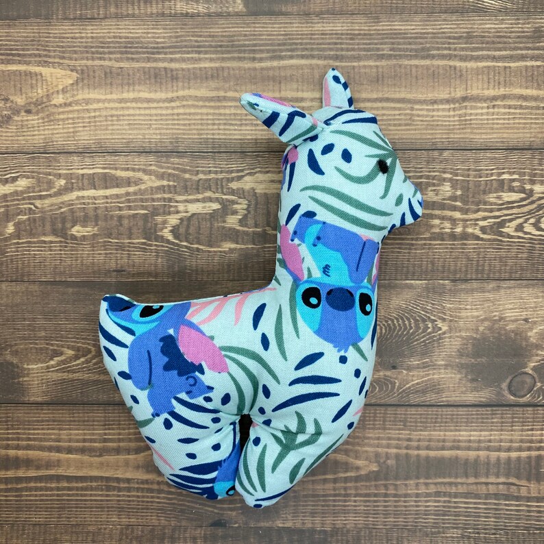 May include: A blue and white plush toy shaped like a llama with a floral pattern and a blue cartoon character on the side.