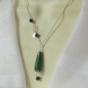 May include: A silver chain necklace with a green teardrop-shaped pendant and black beads. The necklace has a lobster clasp and a small silver charm.