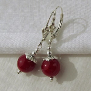May include: A pair of silver dangle earrings with red glass beads. The earrings have a hook fastening.